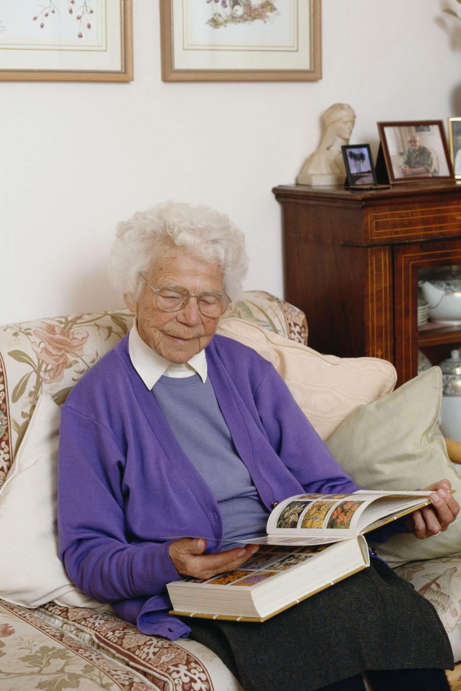 Picture of elderly lady sitting on  a settee  looking through a gardening book
